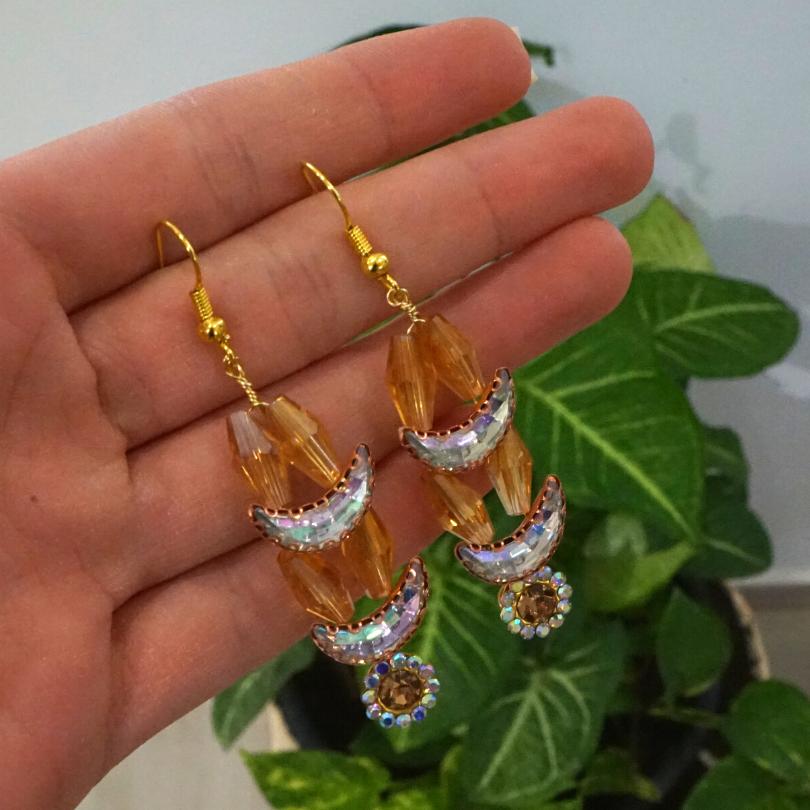 Gold-colored earrings, shaped like crescent moons and golden flowers in pearls